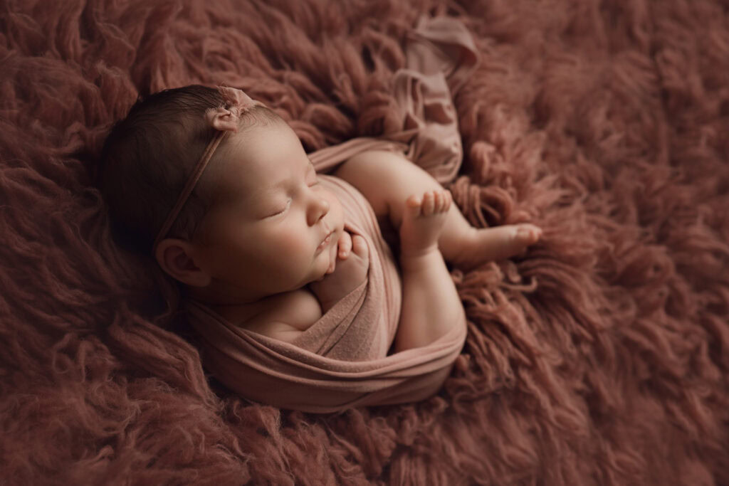 ### Raleigh Newborn Photographer baby girl curled up in pink wrap on pink fur