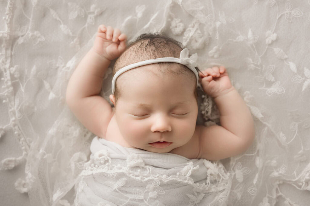 ### Raleigh Newborn Photographer baby girl face forward on white blanket with white lace