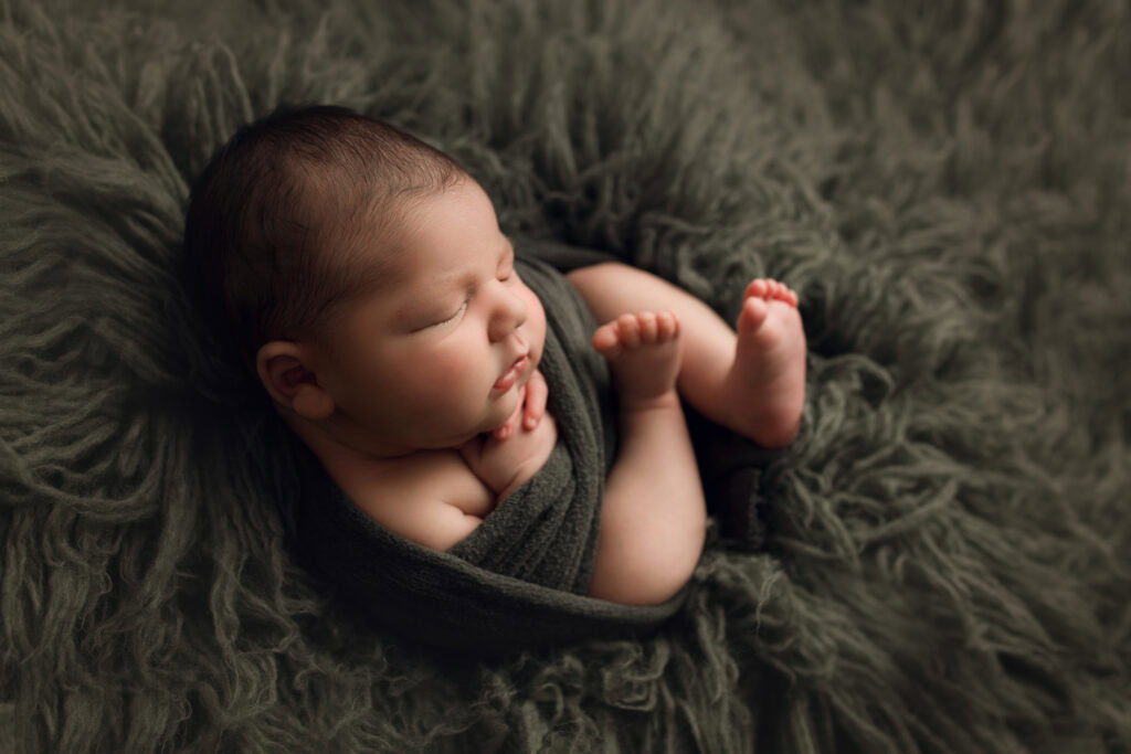 A newborn boy sleeping on a green fur blanket.
