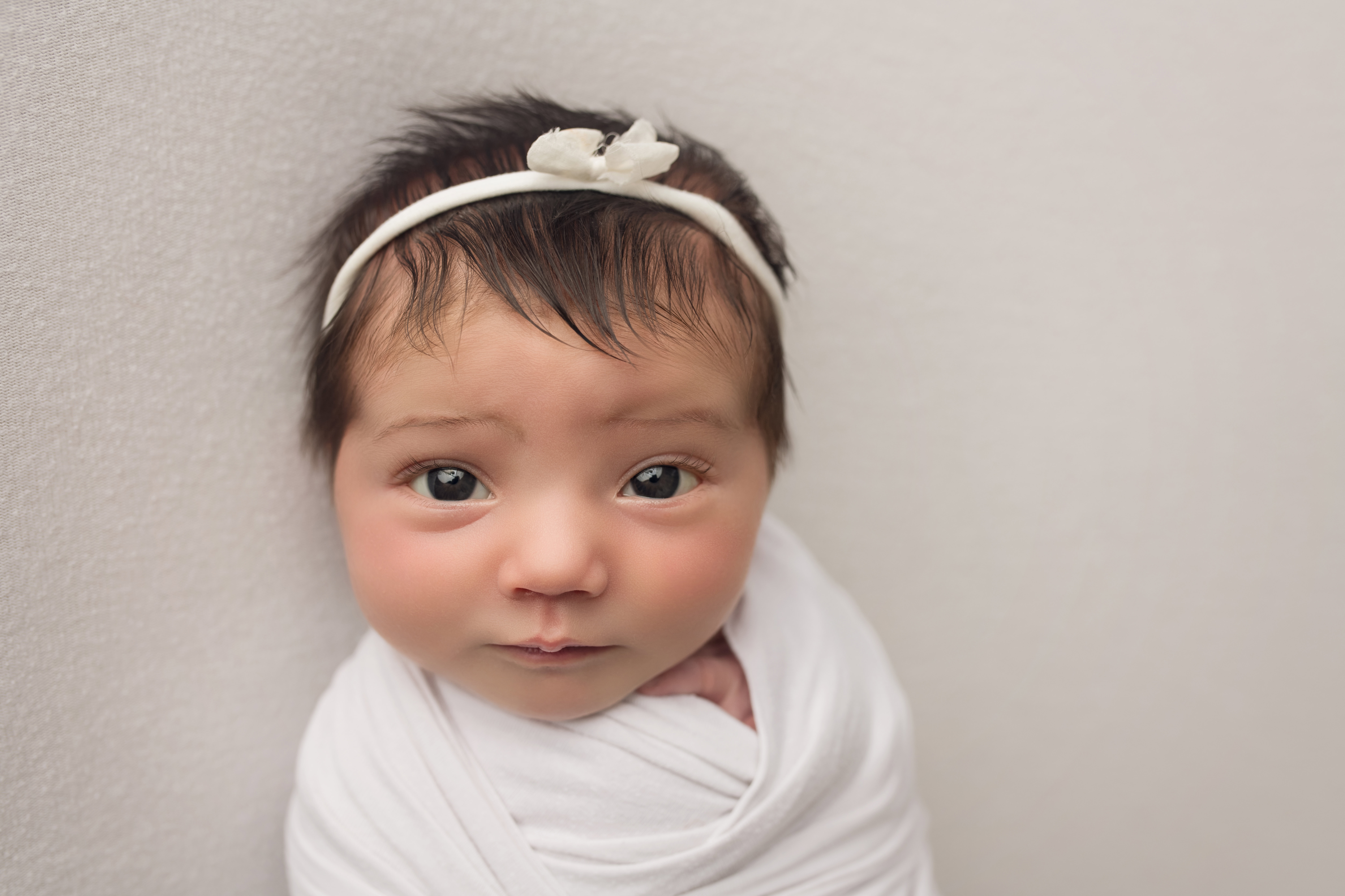 A baby girl in a white wrap with a white headband.