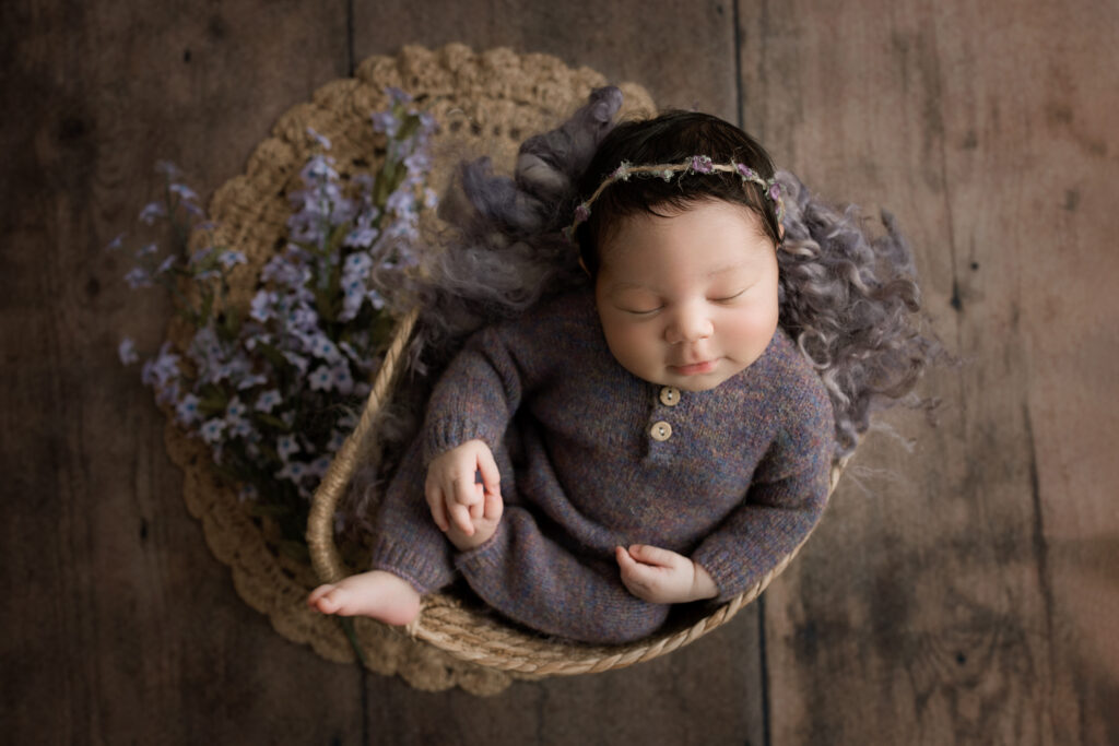 A newborn girl sleeping in a basket on a wooden floor.