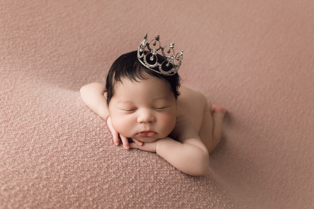 Newborn Baby Girl laying face forward head on hands wearing a princess crown Newborn Photography Raleigh
