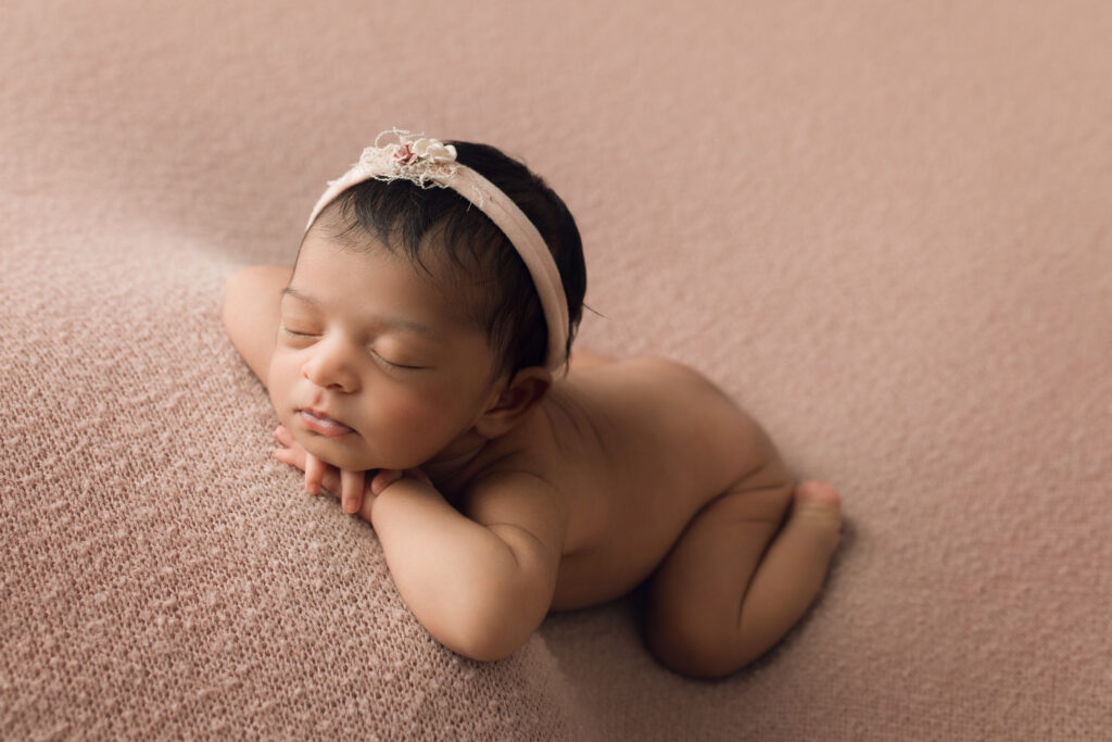 Newborn Baby Girl laying face forward on a pink blanket with matching pink bow Holly Springs NC Newborn Photographer
