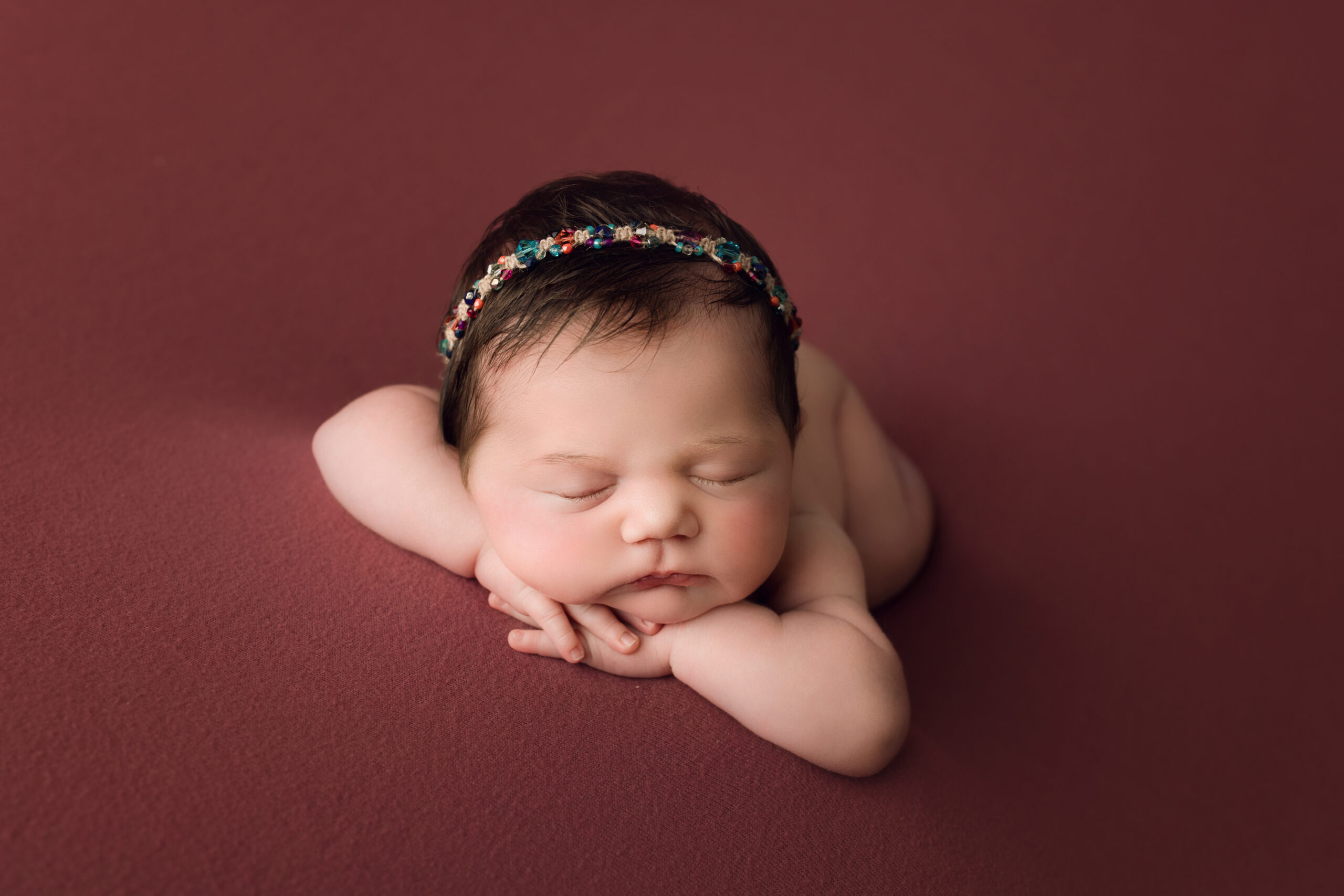 Adorable newborn baby sleeping with headband on dark pink background