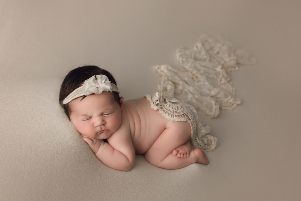 baby newborn sleeping on a beige blanket with lace accessories, peaceful and adorable.