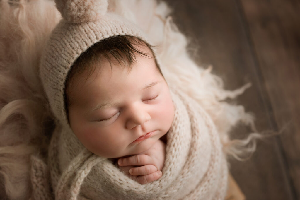 Soft-close-up of a sleeping baby boy wearing a cozy knit hat and blanket, capturing tender newborn photography. Holly Springs NC Newborn Photographer