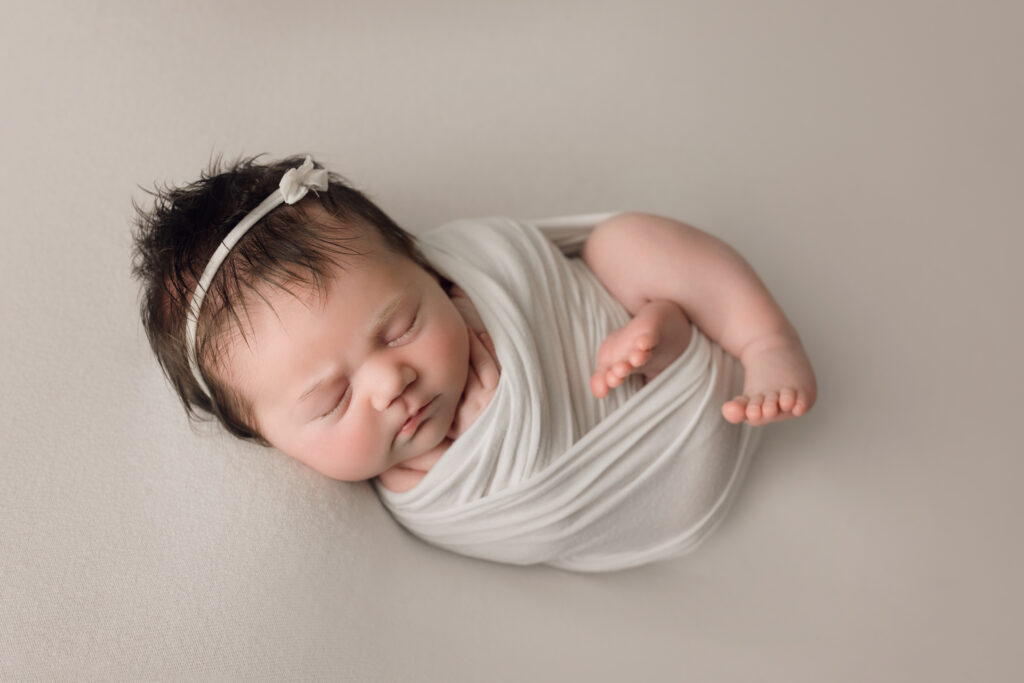 newborn baby girl sleeping, wrapped in white swaddle, lying on white background. Holly Springs NC Newborn Photographer