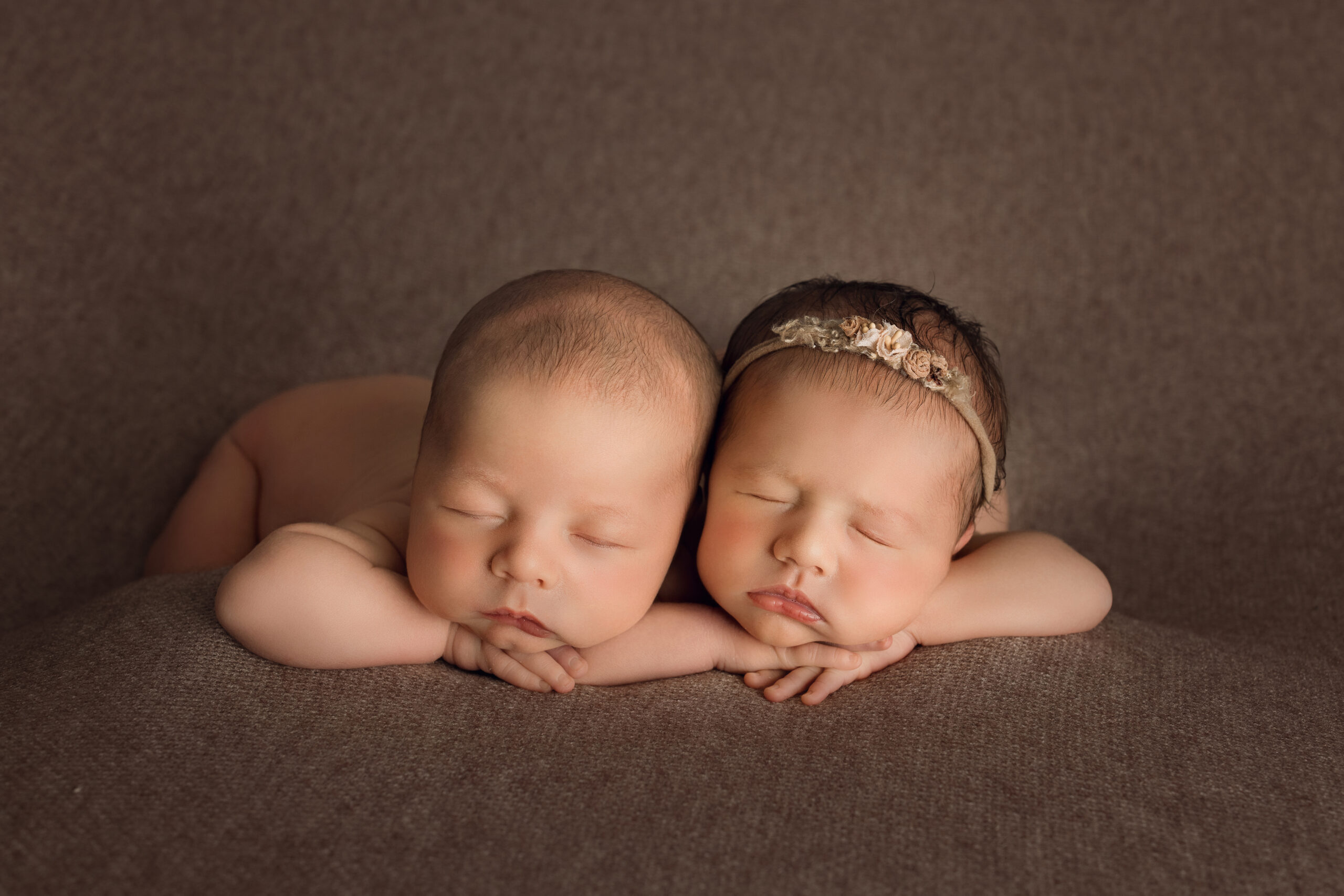 Newborn twin babies sleeping on brown textured background.