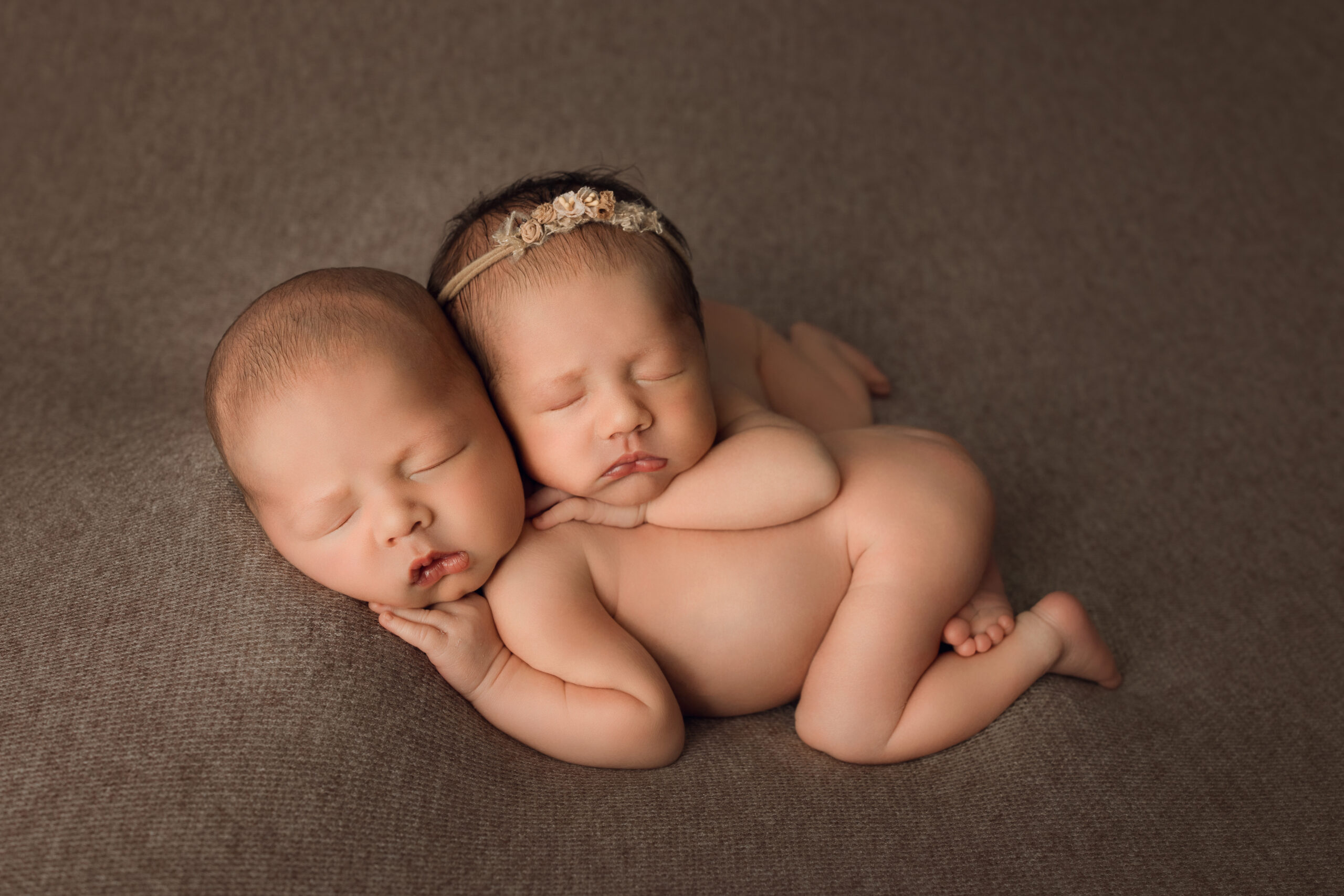 Soft newborn twin siblings sleeping peacefully on textured brown background, capturing adorable infant photography, Newborn Photography, Baby Portraits.