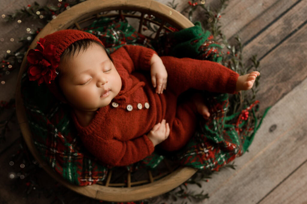 Newborn Baby girl in Christmas bowl and red hat and matching outfit and christmas ornaments and tree