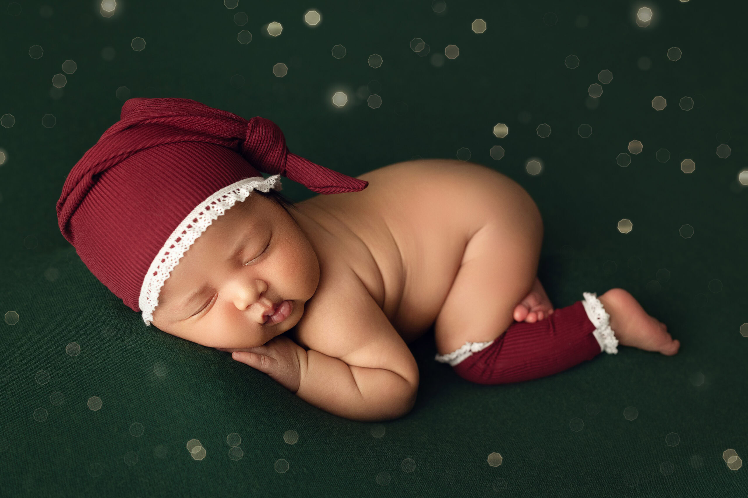 Newborn Baby girl wrapped in green Christmas Wrap on green blanket with Santa Hat and legwarmers