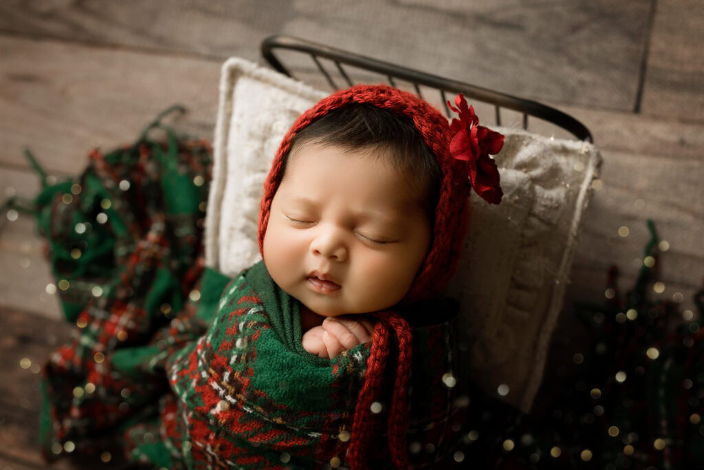 Newborn Baby girl wrapped in green Christmas Wrap in a bed with Christmas Plaid Blanket and christmas tree Micro-Mini Christmas Newborn Session
