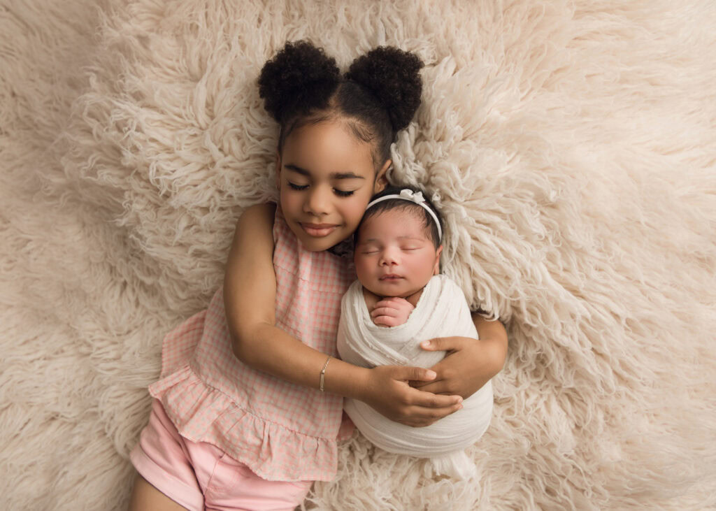 Newborn baby girl wrapped in a cream wrap and matching bowl being snuggled on a cream fur by her beautiful big sister Raleigh Newborn photographer