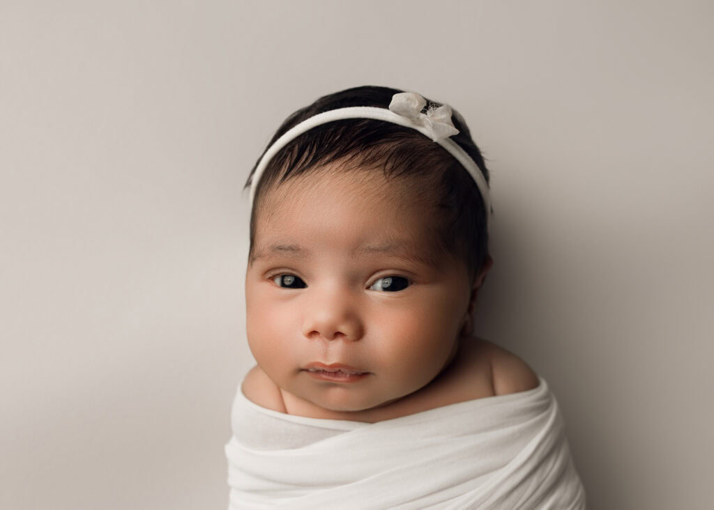 Raleigh Newborn photographer Newborn baby girl wrapped in a white wrap and matching bow on a white background
