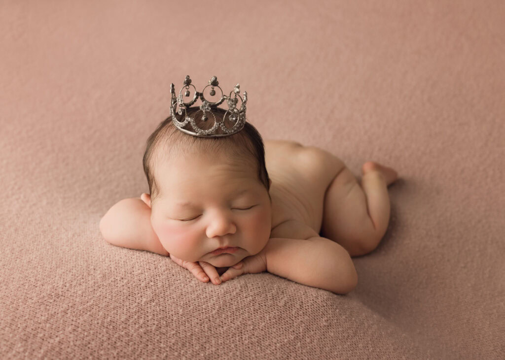 Newborn baby girl sleeping in a face forward pose wearing a princess crown Newborn Photographer