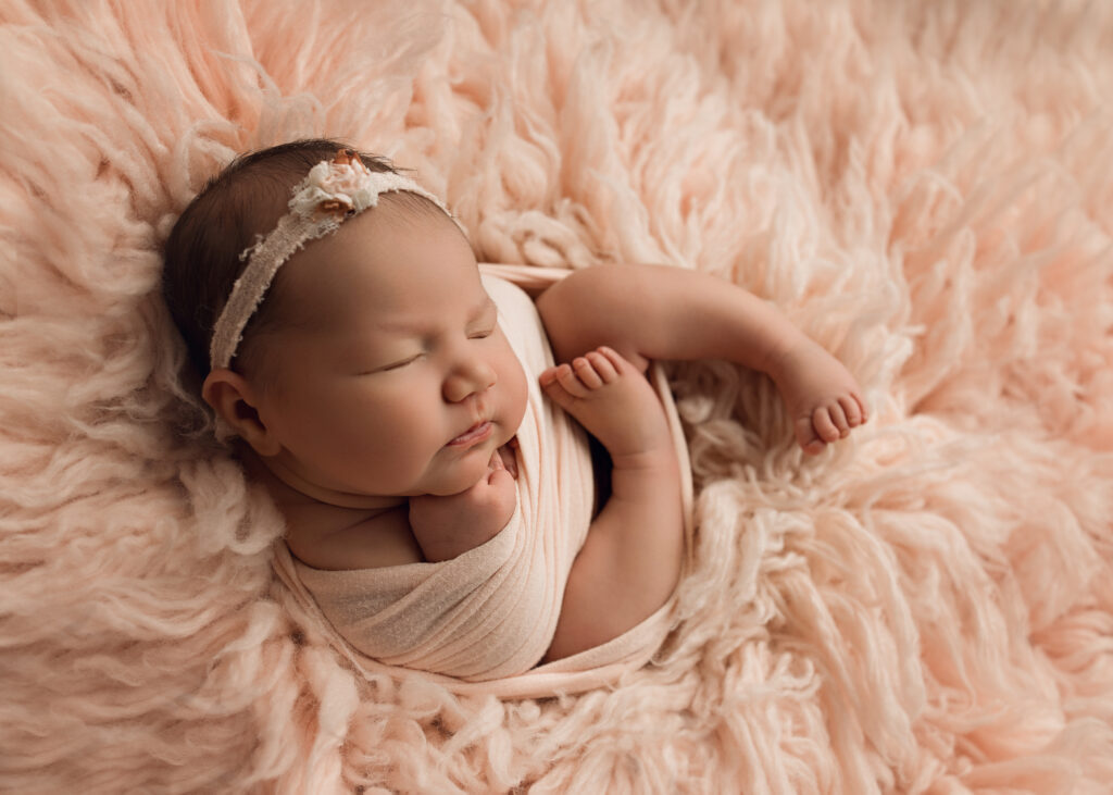 Newborn baby girl sleeping curled up in a pink wrap on pink fur Newborn Photographer